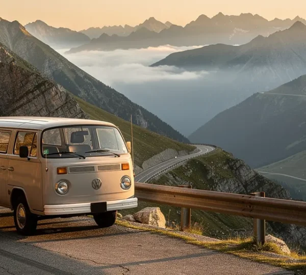 Un van aménagé sur une route sinueuse de montagne avec vue panoramique au lever du soleil, symbolisant la liberté du voyage sur route